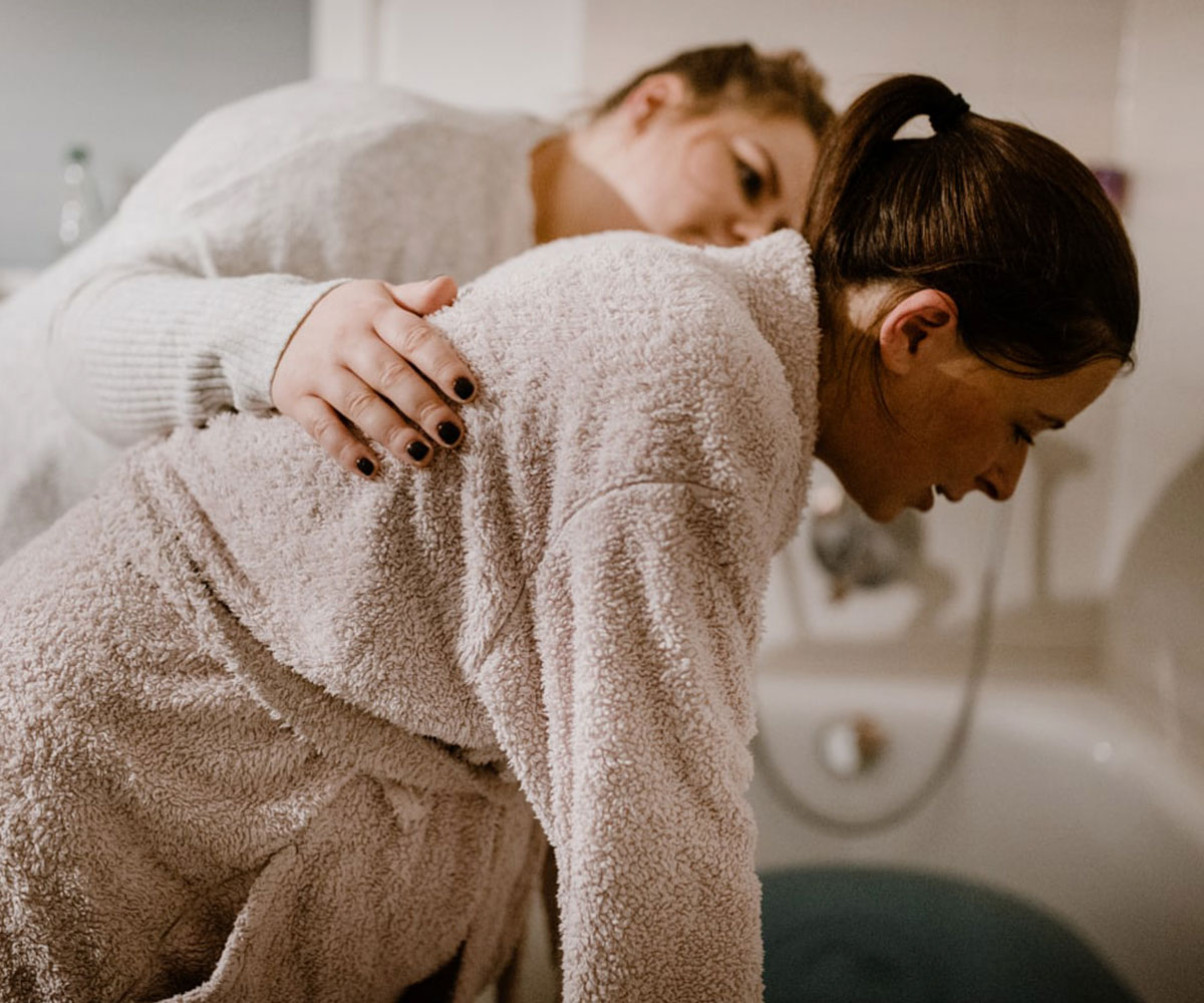 Schwangere steht unter Geburt an der Badewanne, betreut durch Hebammen Vanessa Hildmann